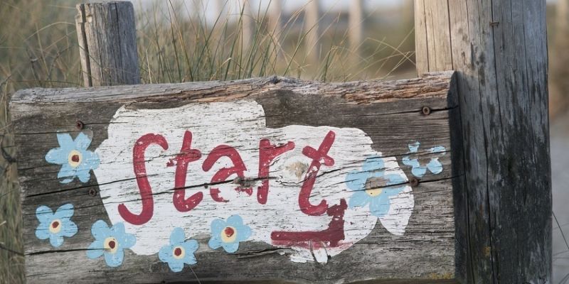 Houten bordje beschilderd met het woord Start versierd met vergeetmenietjes
