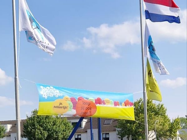 Een avondvierdaagse spandoek geheven tussen twee palen met de Nederlandse vlag