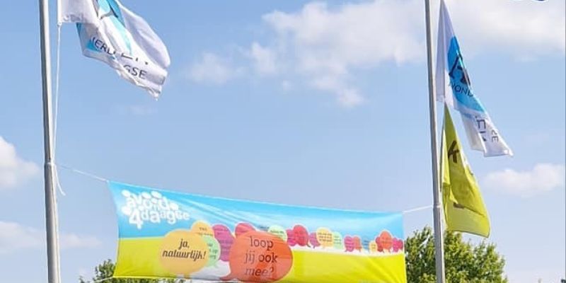 Een avondvierdaagse spandoek geheven tussen twee palen met de Nederlandse vlag